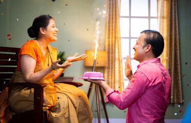 Happy Husband celebrating excited wife birthday by giving surprise cake for celebration at home -...