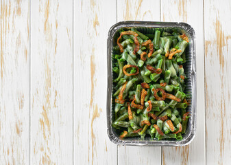 green bean casserole with crispy fried shallots onion in a disposable square aluminium foil baking...
