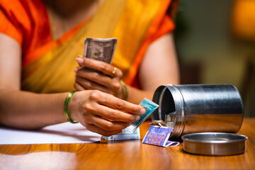 Close up shot of woman counting money by taking from steel box for monthly expenses at home -...