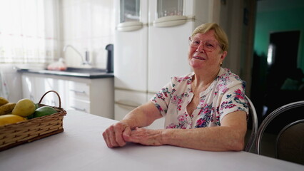 Fototapeta na wymiar Happy senior woman smiling at camera in authentic domestic lifestyle. A caucasian elderly person in 80s smiling at camera while sititng at kitchen