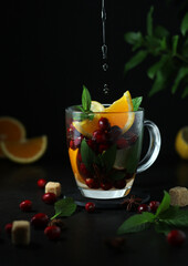 Hot tea pouring into transparent glass tea with cranberry and orange