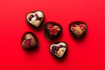 chocolate sweets in the form of a heart with fruits and nuts on a colored background. top view with space for text, holiday concept
