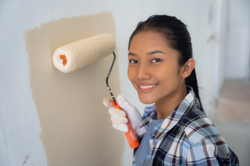 Young asian woman enjoying renovation time at home while holding roller. Repair and remodeling concept.