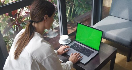Young woman using laptop with green screen while sitting in modern cafe with coffee. Young business woman at coffee shop working on a Laptop Computer with Green Mock-up Screen. Chroma key, copy space - Powered by Adobe