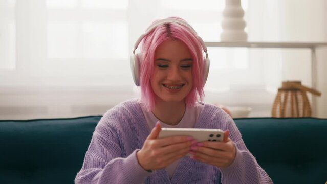 Smiling pink-haired woman in headphones watching music video on smartphone, app