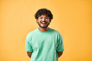 Candid portrait of a handsome curly-haired young man in a turquoise t-shirt and glasses on a yellow...