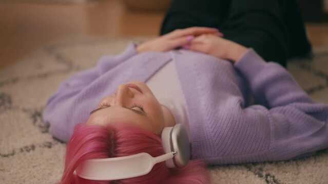 Calm young woman in headphones lying on floor and enjoying music, resting home