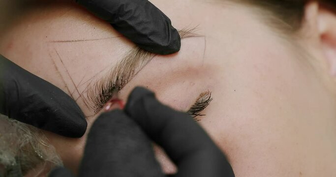 Microblading, permanent makeup tattoo close up. The master makes permanent eyebrow makeup with a needle tattoo machine. Microblading brows tattooing. Dark pigment is injected under skin.
