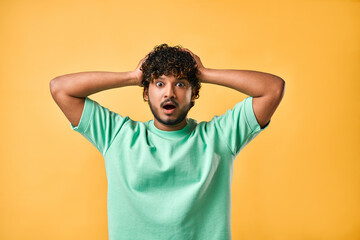 Portrait of a handsome young man in a turquoise T-shirt on a yellow background holding his head and...