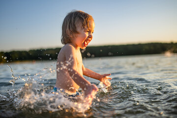 Cute toddler boy playing by a lake on hot summer day. Adorable child having fun outdoors during summer vacations.