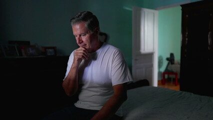 Thoughtful older man sitting by bedside with pensive expression. Domestic lifestyle of middle-aged person pondering solution to problem