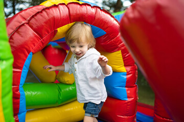 Fototapeta na wymiar Cute toddler boy jumping on a inflatable bouncer in a backyard on warm and sunny summer day. Sports and exercises for children.