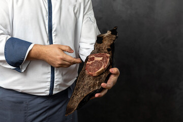 Crop anonymous male in uniform holding piece of fresh delicious meat on wooden board against grunge black background