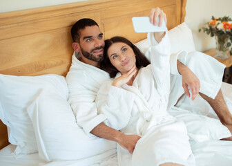 Happy couple resting in hotel room taking selfie via phone
