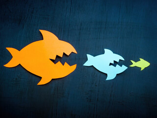 Paper fish are trying to eat each other. Concept of merger and acquisition or competition.