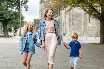 Young adult beautiful mom enjoy having fun walking with two kids in european city street at summer...