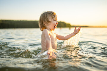 Cute toddler boy playing by a lake on hot summer day. Adorable child having fun outdoors during summer vacations.