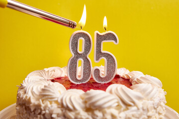 A candle in the form of the number 85, stuck in a festive cake, is lit. Celebrating a birthday or a...