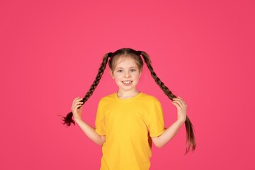 Portrait of cute cheerful little girl with braids posing over pink background,