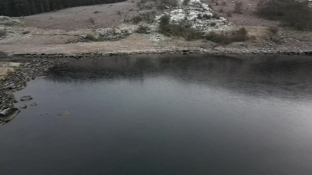 Drone shot over Capel Curig lake with frozen edges in winter and mountain in the background