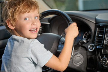 a cute boy is sitting in a car with a black interior, holding the steering wheel and looking at the...