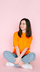 Fototapeta premium Dreaming in Serenity: Beautiful Woman Seated Comfortably in Lotus Position, Gazing into Empty Space, Yearning for a New Love - Tranquil Mood on Pink Background.