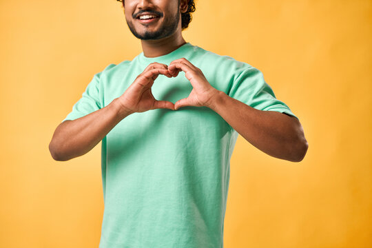 Cropped image of an Indian man in a turquoise T-shirt showing a gesture of heart, love, affection, care with his fingers.