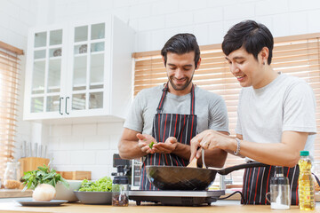 LGBTQ+ gay bisexual cooking their meal together in the kitchen, LGBTQ gay couple making a spaghetti. A different ethnicity handsome gay couple enjoy cooking a spaghetti together in kitchen.