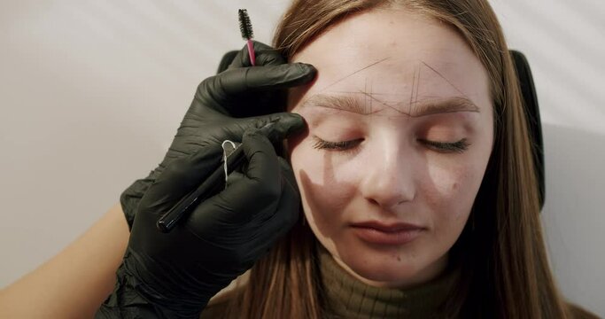 Cosmetologist marks the lines with a special thread to create the correct shape of the eyebrows. Permanent makeup process. Cosmetologist making eyebrow permanent makeup. Work of master cosmetologist.