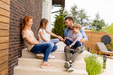 Family with a mother, father, son and daughter sitting outside on the steps of a front porch of a brick house