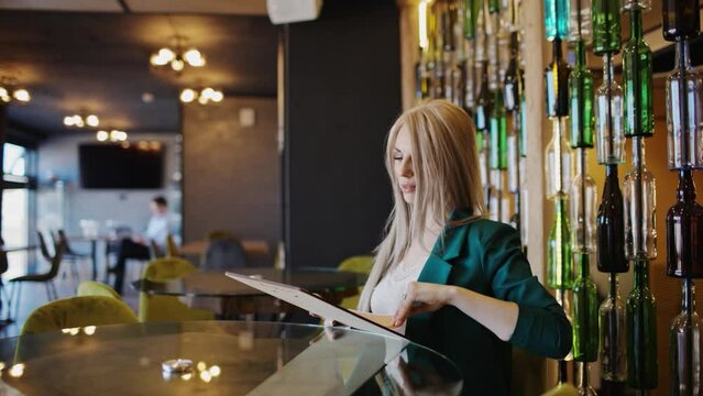 A blonde woman in a green jacket selects the food menu for dinner at a downtown wine restaurant