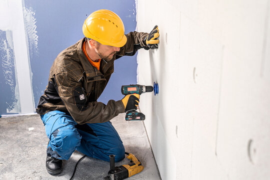 A construction worker working with a cordless drill at milling hole to mineral insulation board for insert a dowel.