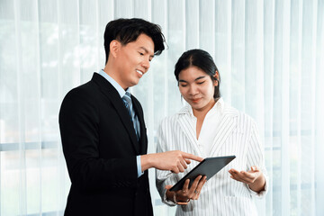 Manager advising guiding younger colleague with tablet in workplace. Couple businesspeople in...