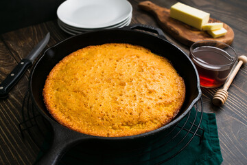 Buttermilk Cornbread Baked in a Cast-Iron Skillet at a Low Angle: Freshly made Southern cornbread in a frying pan with butter and honey on the side
