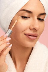 Smiling woman in bathrobe applying concealer on face