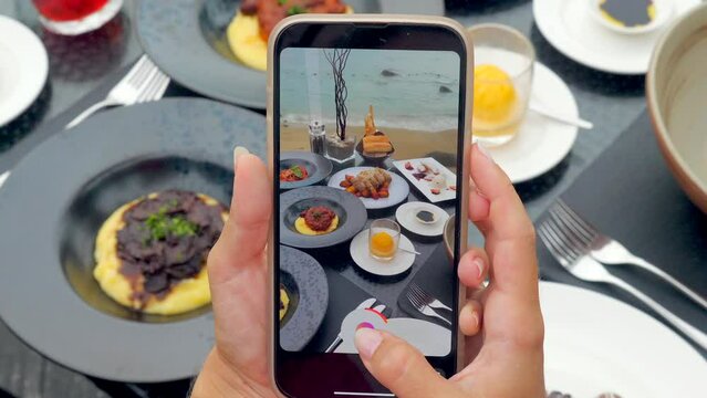 Closeup of a woman hands using a smartphone to capture videos or photos of her dinner in an outdoor tropical restaurant.