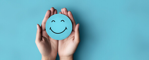 Promoting Positive Mental Health: Hand Holding Blue Paper Cut Happy Smile Face for World Mental Health Day - obrazy, fototapety, plakaty