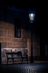 Fototapeta na wymiar Vertical of a lantern illuminating empty bench against a stone house at night in Copenhagen, Denmark