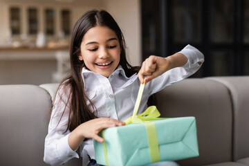 Happy Kid Girl Opening Present Box Celebrating Holiday At Home