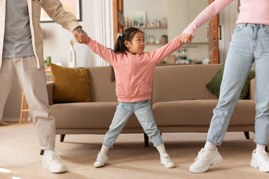 Asian Parents Pulling Daughter's Hands In Different Directions Standing Indoor