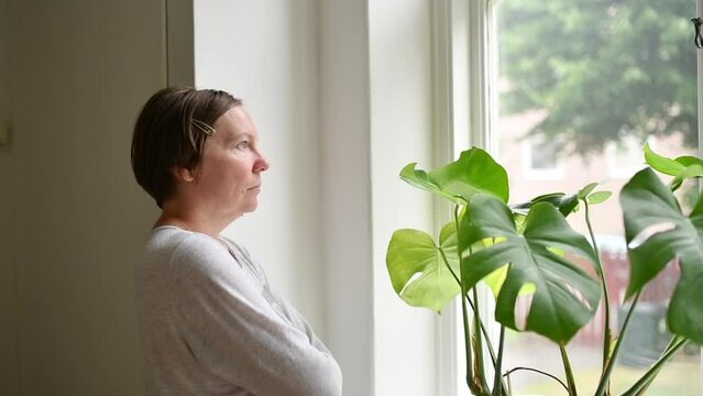 Introspective mid-adult female person looking out the window and contemplating
