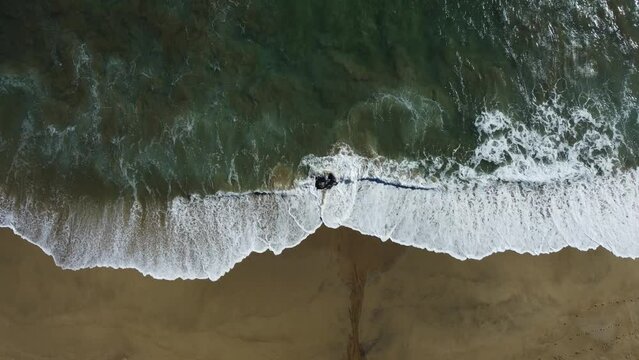 Aerial view of the foamy sea waves splashing over the shore on Zapallar beach, Chile