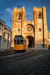 Naklejka na ściany i meble Vertical shot of the Lisbon Cathedral as a tram is passing in front of it