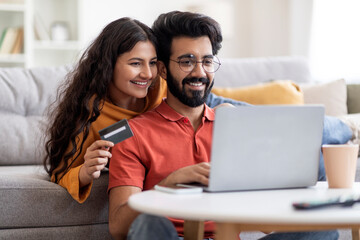 Online Auction. Indian Couple With Laptop And Credit Card Making Internet Bids