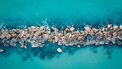 Aerial top view of a pebbled island in the middle of a turquoise sea on a sunny day