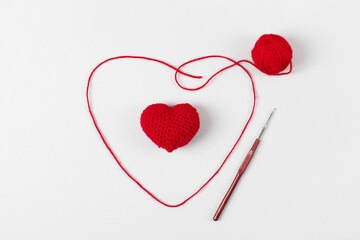 Crocheted red heart on a gray background and and a ball of thread with a hook. Symbol of love. Top view, flat lay