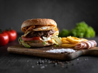 Closeup of a burger with French fries on a wooden board.