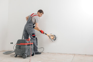 Man worker Painter work with white wall polishing and sanding surface after putty for painting in new apartment