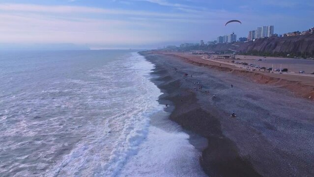 Aerial view of splashing waves coastal beach with Paragliding activity in Lima