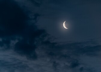Naklejka na ściany i meble Beautiful shot of a half moon illuminating a dark blue cloudy sky